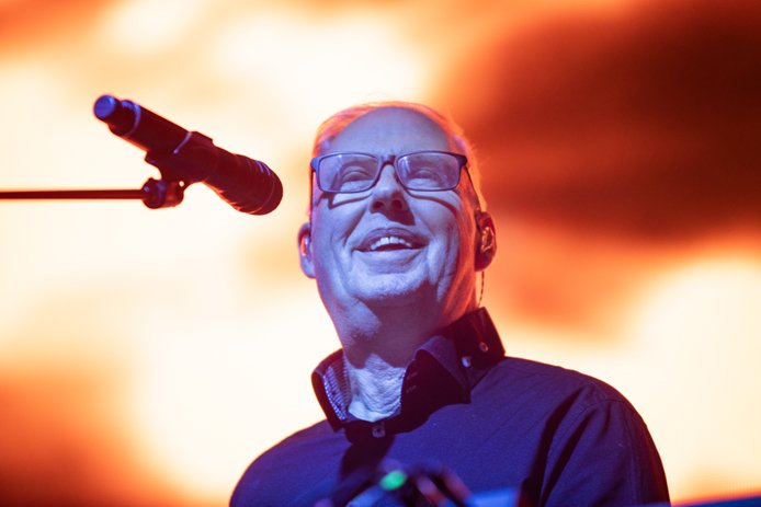 Paul Humphreys i OMD smiler på scenen, ved en mikrofon