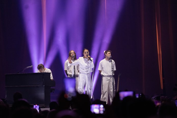 Highsakite samlet på en catwalk foran et teppe på en scene. Ingrid Helene Håvik synger med armen utstrakt
