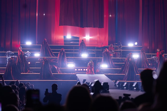 Masse kappekledte figurer på en svær scene, rundt Highasakite, med Ingrid Helene Håvik i midten